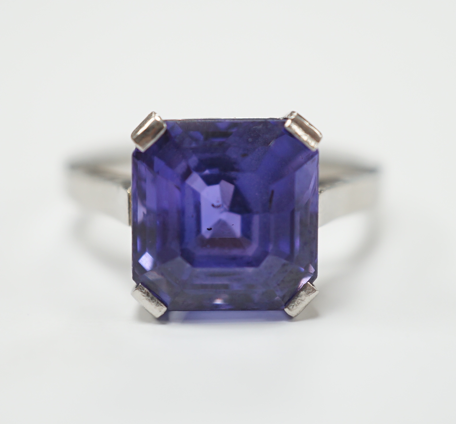 A white metal and single stone and square cut blueish purple sapphire set dress ring, size M, gross weight 5.6 grams, the stone measuring 10mm by 9,8mm, with a depth of 7.4mm.